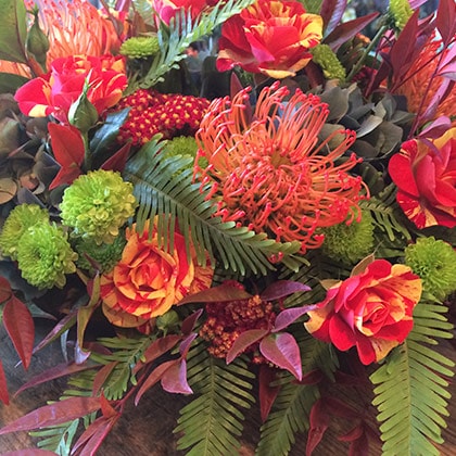 Chartreuse button mums, orange pin cushion proteas, crazy two spray roses mixed with red yarrow and umbrella fern in this stunning flower arrangement. 