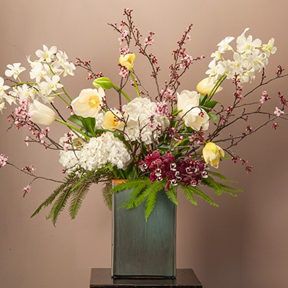 Flowering Plum branches mixed with cut white dendrobium orchids, tulips and umbrella fern grace the edges of this large stand flower arrangement.