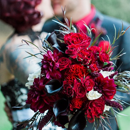 An October wedding bouquet with roses, dahlias and Adonis foliage complete the red, burgundy theme.
