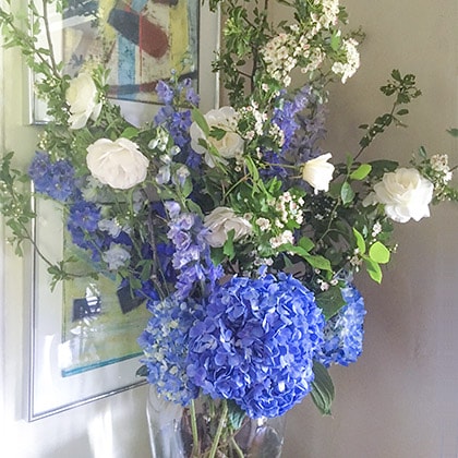 Spring is welcomed by white Hawrhorne branches and blue delphinium mixed with Iceberg roses and a beautiful shade of blue hydrangea complete this flower arrangement.