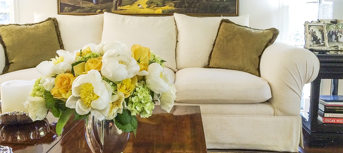 Spring flower arrangement for a living room features white peonies with yellow stamens, white roses mixed with yellow roses and luscious green hydrangeas in a silver vase.
