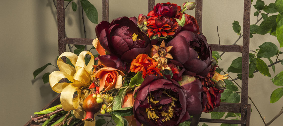 Hand tied bridal bouquet with dark burgundy peonies, rusty orange ranunculus, orange “Brandy” garden roses and mini pomegranates.