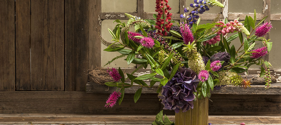 Early summer flower arrangement with pink hebe, Peruvian pineapple and dark artichokes mixed with lupine.